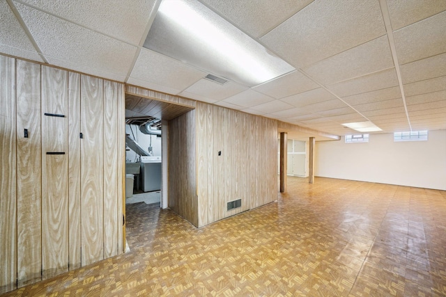 basement featuring washer / dryer, visible vents, wood walls, and a paneled ceiling