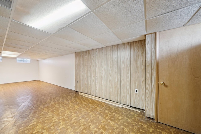 below grade area featuring a paneled ceiling and wood walls