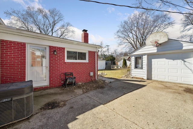 exterior space featuring brick siding, concrete driveway, central AC, a chimney, and a garage