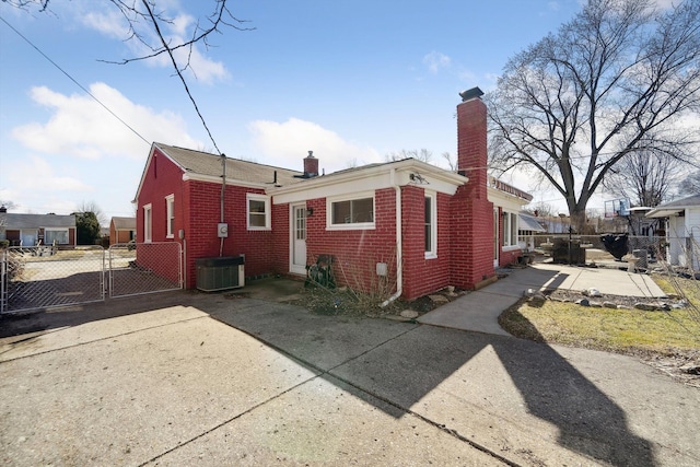 rear view of property with a gate, fence, cooling unit, a chimney, and brick siding