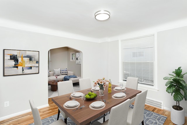 dining space with baseboards, visible vents, arched walkways, and wood finished floors