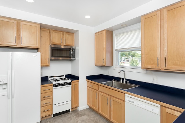 kitchen featuring light brown cabinets, white appliances, dark countertops, and a sink