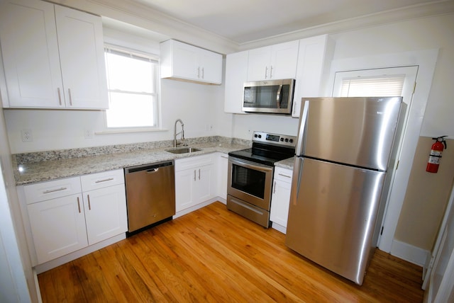 kitchen with light stone counters, light wood finished floors, appliances with stainless steel finishes, white cabinetry, and a sink