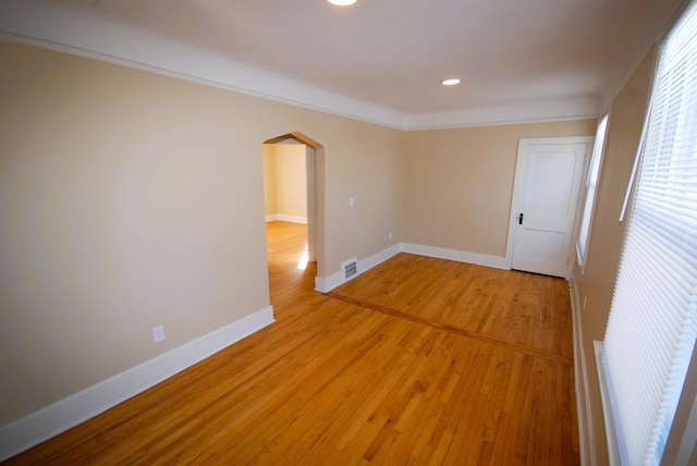 empty room featuring light wood finished floors, baseboards, visible vents, arched walkways, and ornamental molding