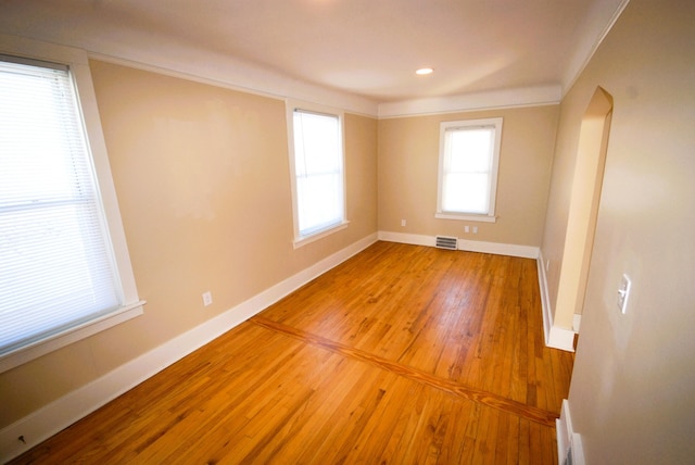 empty room featuring ornamental molding, light wood-type flooring, visible vents, and baseboards