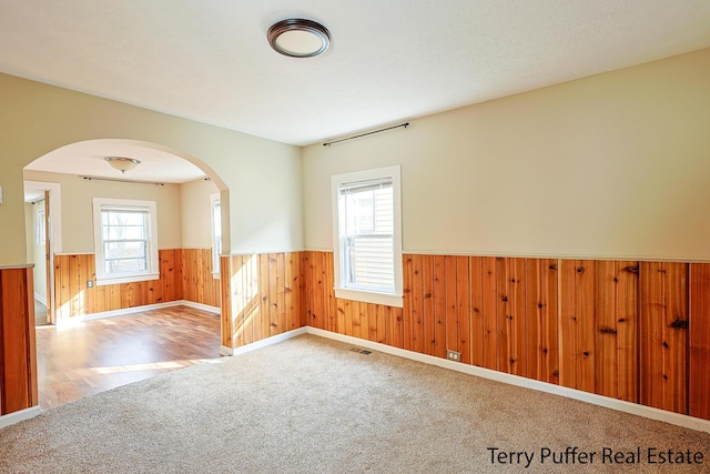 carpeted empty room featuring visible vents, arched walkways, and a wainscoted wall