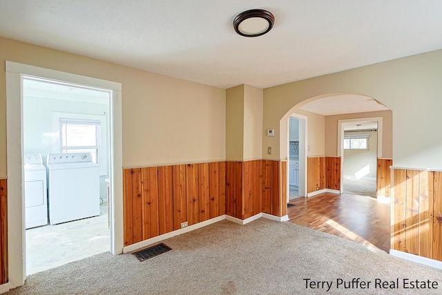 carpeted empty room with washing machine and clothes dryer, wooden walls, visible vents, a wainscoted wall, and arched walkways