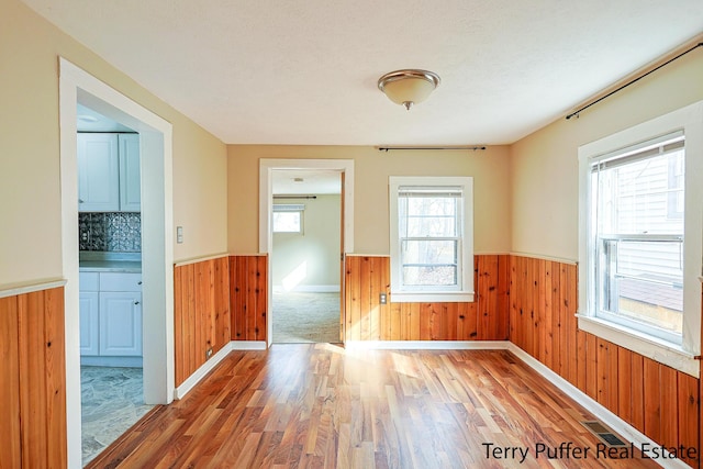 unfurnished room with wooden walls, wainscoting, and light wood-style floors