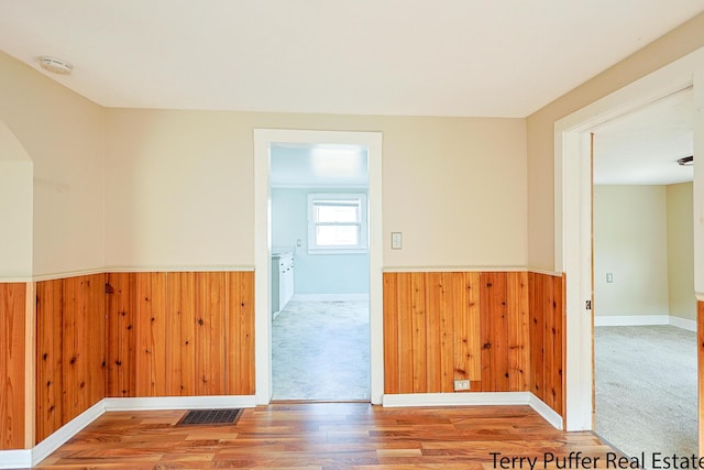 unfurnished room featuring wooden walls, a wainscoted wall, visible vents, and wood finished floors