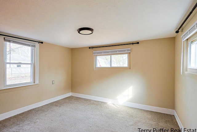 carpeted empty room featuring baseboards, a textured ceiling, and a healthy amount of sunlight