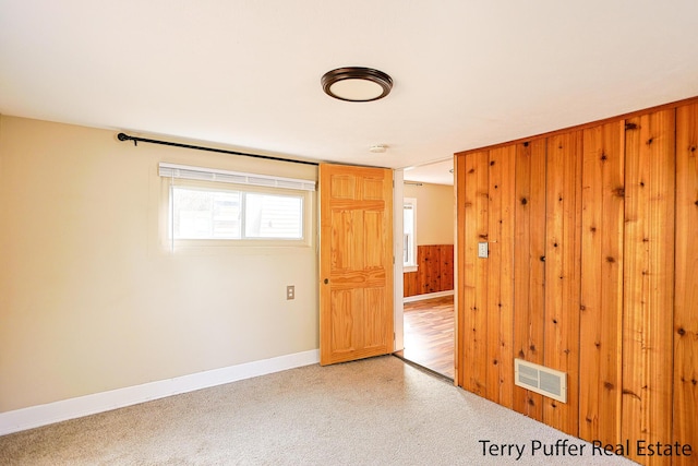 unfurnished room featuring visible vents, baseboards, wooden walls, and light colored carpet