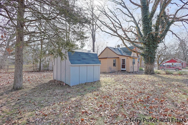 exterior space with a storage unit, an outbuilding, a fenced backyard, and a shingled roof