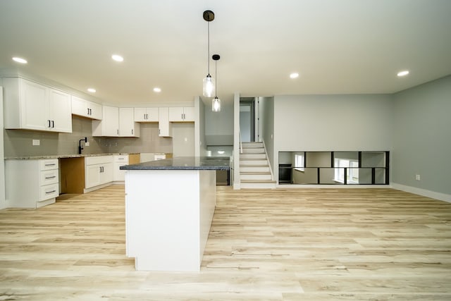 kitchen with light wood finished floors, a kitchen island, white cabinetry, and backsplash