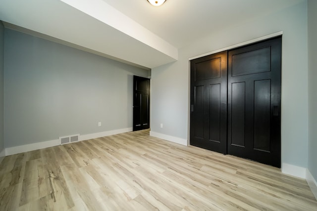 unfurnished bedroom with a closet, light wood-type flooring, visible vents, and baseboards