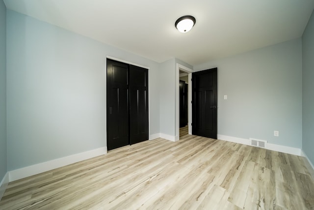 unfurnished bedroom featuring baseboards, a closet, visible vents, and wood finished floors