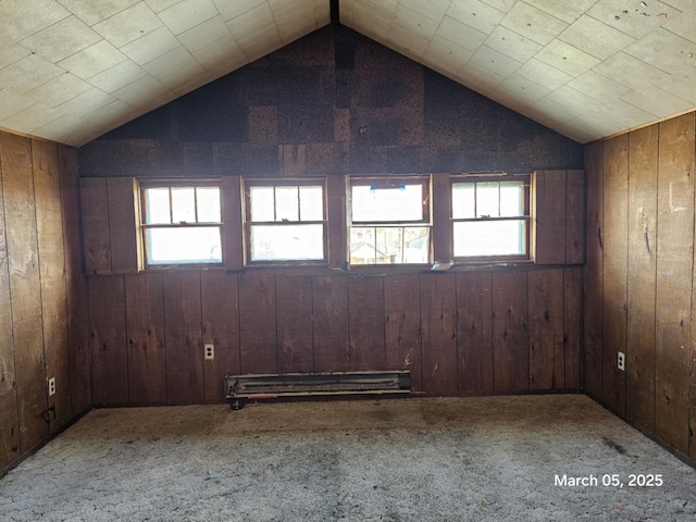 carpeted empty room with a baseboard radiator, vaulted ceiling, and wood walls