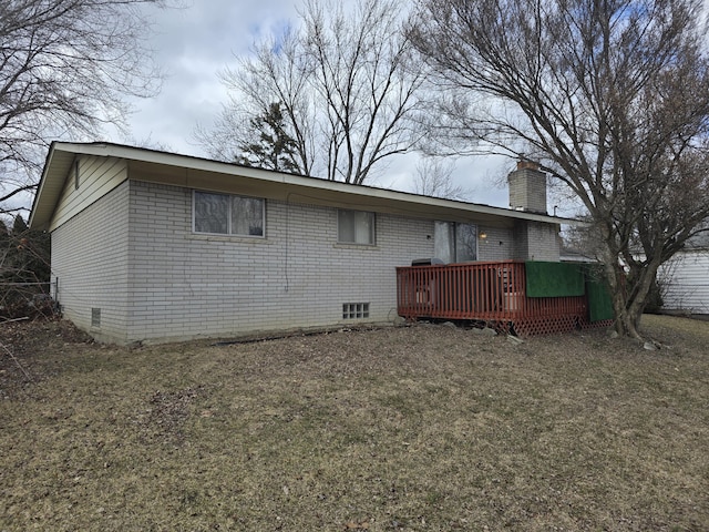 rear view of property featuring a deck, brick siding, a chimney, and a lawn