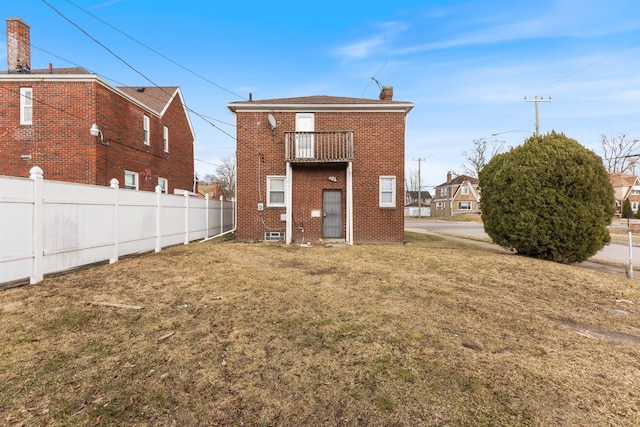 rear view of house with a balcony, fence, a chimney, a lawn, and brick siding