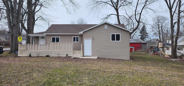 back of house with a shingled roof, a deck, and a yard