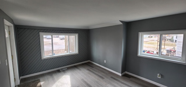 spare room with a healthy amount of sunlight, visible vents, baseboards, and wood finished floors