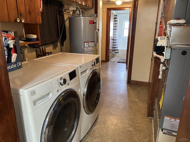 clothes washing area featuring washing machine and clothes dryer, baseboards, light floors, water heater, and cabinet space