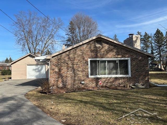 view of home's exterior with driveway, an attached garage, a chimney, a lawn, and brick siding