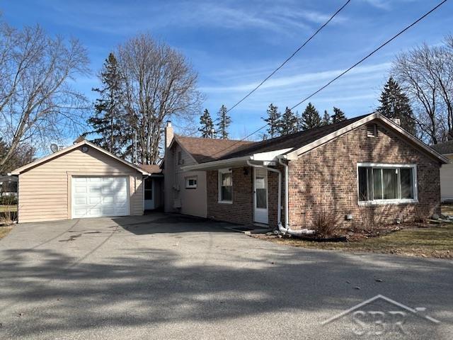 single story home featuring an attached garage, brick siding, a chimney, and driveway