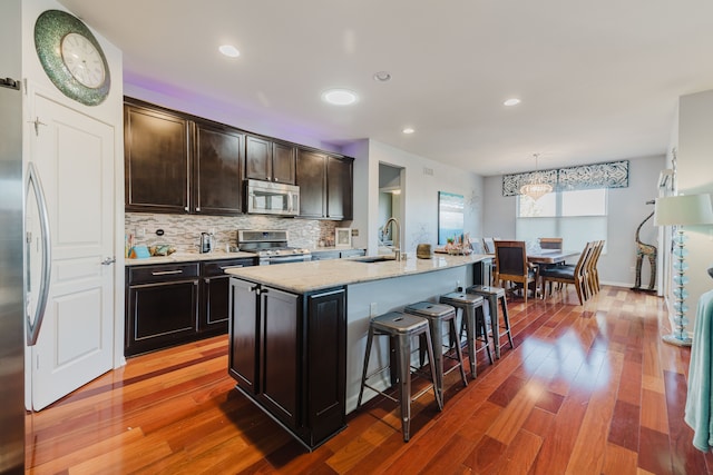 kitchen with a kitchen bar, a sink, appliances with stainless steel finishes, light wood finished floors, and decorative backsplash