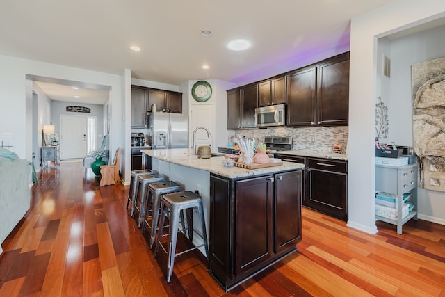 kitchen featuring light stone countertops, dark brown cabinetry, appliances with stainless steel finishes, a kitchen breakfast bar, and tasteful backsplash