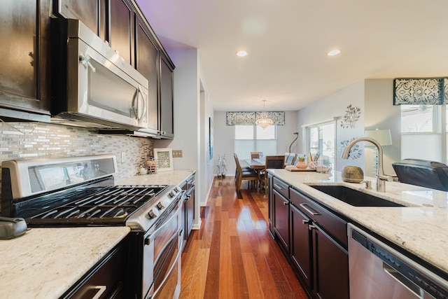 kitchen featuring dark wood-style floors, light stone countertops, a sink, stainless steel appliances, and backsplash