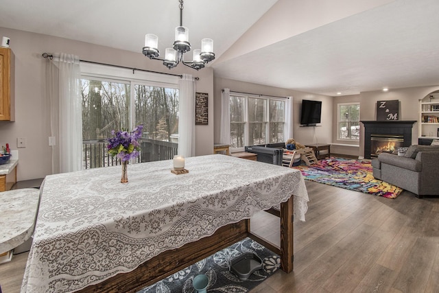 dining space with an inviting chandelier, vaulted ceiling, wood finished floors, and a glass covered fireplace