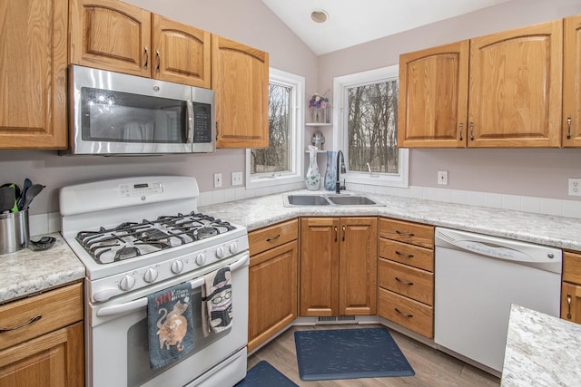 kitchen with lofted ceiling, white appliances, a sink, light countertops, and light wood finished floors