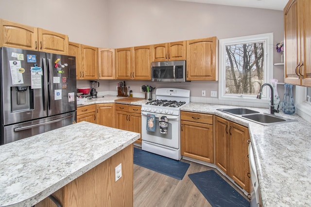 kitchen with high vaulted ceiling, a sink, light countertops, appliances with stainless steel finishes, and light wood finished floors