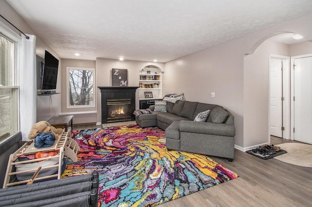 living area with arched walkways, a textured ceiling, wood finished floors, a fireplace with flush hearth, and baseboards