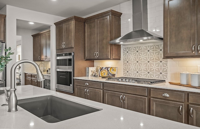 kitchen featuring a sink, appliances with stainless steel finishes, wall chimney exhaust hood, and dark brown cabinets