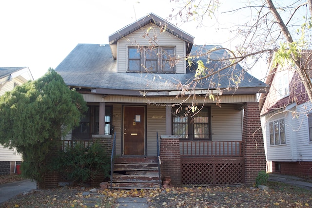 view of front of house featuring a shingled roof, a porch, and brick siding