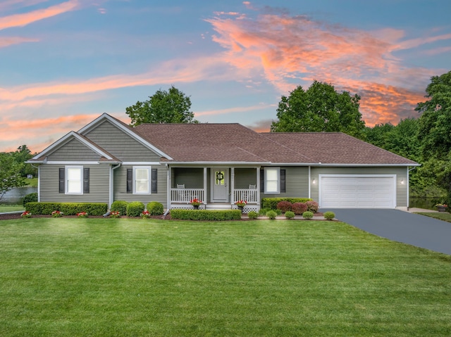 ranch-style house featuring driveway, roof with shingles, an attached garage, covered porch, and a lawn