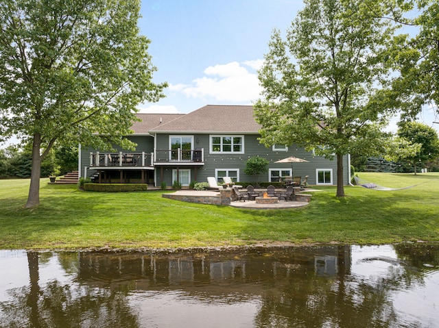 back of house with a deck with water view, a patio, a lawn, and an outdoor fire pit