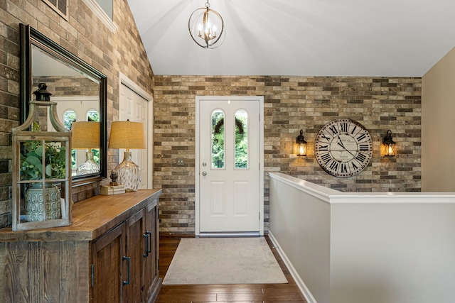 foyer entrance with lofted ceiling, an inviting chandelier, dark wood-style floors, and brick wall