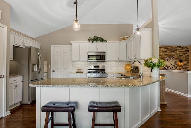 kitchen featuring light stone countertops, a peninsula, a sink, vaulted ceiling, and appliances with stainless steel finishes