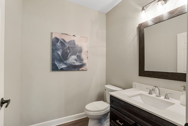 half bathroom with baseboards, toilet, wood finished floors, and vanity