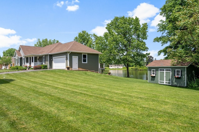 view of front of house featuring a front yard, an attached garage, a water view, and an outdoor structure