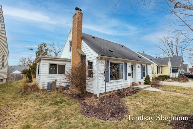 view of front of house featuring central air condition unit, a shingled roof, fence, a chimney, and a front yard