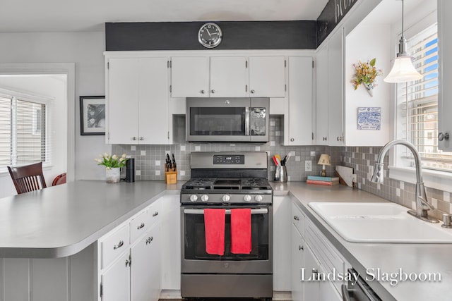 kitchen with a peninsula, stainless steel appliances, light countertops, white cabinetry, and a sink