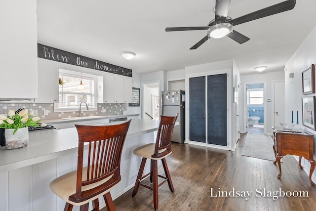 kitchen with a breakfast bar, light countertops, freestanding refrigerator, tasteful backsplash, and dark wood finished floors