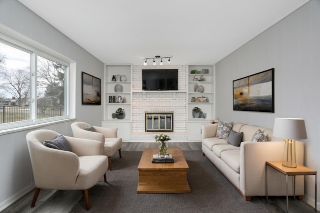 living room featuring rail lighting, a brick fireplace, built in features, and wood finished floors