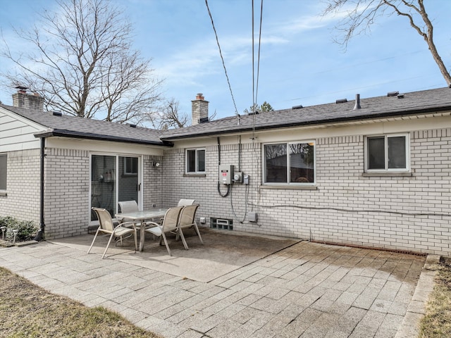 rear view of property featuring a patio area, a chimney, brick siding, and roof with shingles