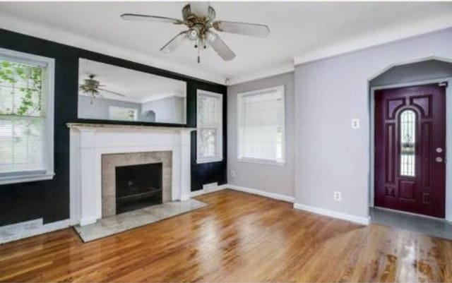 unfurnished living room featuring plenty of natural light, baseboards, a fireplace with flush hearth, and wood finished floors