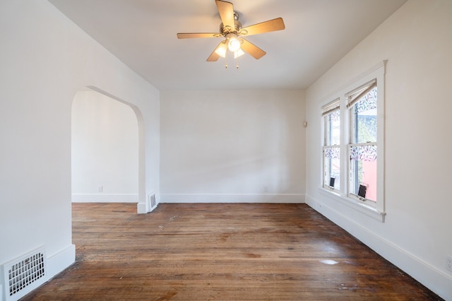 empty room featuring wood finished floors, arched walkways, visible vents, and baseboards