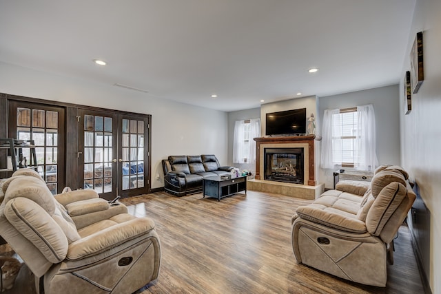 living area with a tile fireplace, recessed lighting, french doors, and wood finished floors